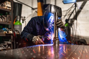 Sadece metal fabrikasında koruyucu eldiven ve maske takan konsantre bir erkek işçi.