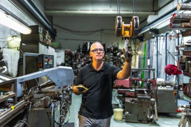 Metal atölyesinde elektrikli vinç kullanan yetişkin bir erkek işçi.