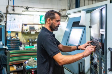 Mature man working on control panel of a lathe in cnc factory clipart