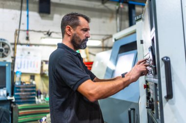 Side view of a mature caucasian man working in the control station of a cnc factory clipart