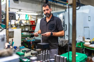 Beyaz erkek operatör mikrometre kullanarak fabrikadaki metal parçaları üzerinde kalite kontrolü yapıyor.