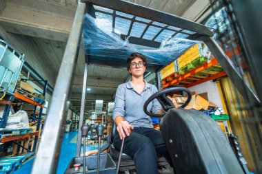 Metalurji fabrikasında çalışan beyaz bir kadının ön cepheden düşük açılı görüntüsü. Forklift kullanıyor.