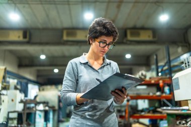 Bir fabrikada envanter sayımı yaparken beyaz kadın yöneticinin ön cepheden düşük açılı görüntüsü.