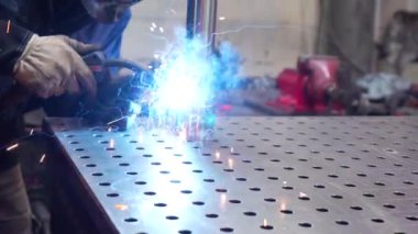 Fabrikada çalışan yüz maskesi ve güvenlik önlüğü takan bir kaynakçının üç çeyrek uzunluğundaki videosu.
