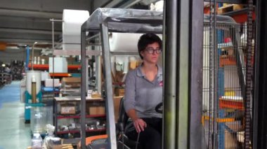 Metalurji fabrikasında çalışan beyaz bir kadının ön cepheden düşük açılı görüntüsü. Forklift kullanıyor.