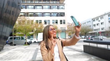 Latin bir kadın bir şehri ziyaret ediyor ve cep telefonuyla fotoğraf çekiyor. Günün tadını çıkarıyor.