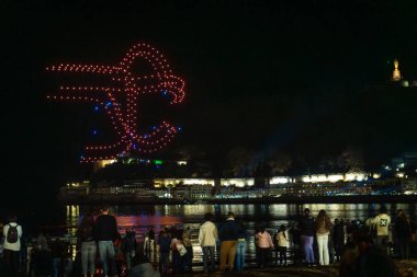 Drone show at night during the Christmas inauguration in San Sebastian, Gipuzkoa. Illuminated city and the figure of the wind comb by Eduardo Chillida clipart