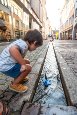 Çocuk yazın Almanya 'da Freiburg im Breisgau kanalında tekneyle oynuyor.