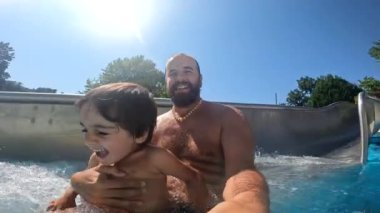 Bir adam ve bir çocuk kaydırak kayıyor. Çocuk gülümsüyor.