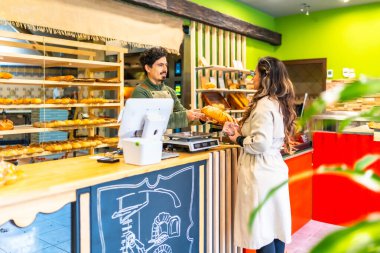 Latin genç satıcı bir fırında kadın müşteriye ekmek veriyor.