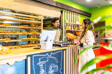 Kadın tezgahın yanında satıcıyla konuşurken fırından ekmek alıyor.