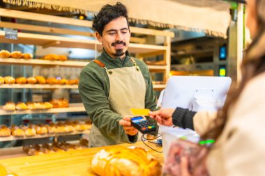 Modern bir fırında kredi kartı kullanan Latin bir kadının arka görüntüsü.