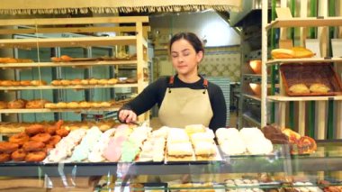 Bir pastanede satmak için renkli hamur işleriyle dolu tezgahın yanındaki Latin satıcı kadın.