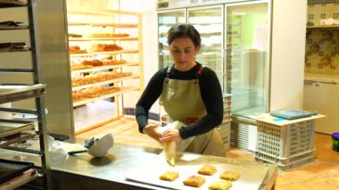 Bir fırının atölyesindeki pastaları süslemek için boru torbası dolduran Latin bir fırıncı kadın.