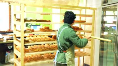 Latin bir adamın fırındaki rafa fırınlanmış zanaatkar ekmeği koyuşunun arka görüntüsü.