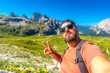 İtalya Alplerinde yaz yürüyüşü sırasında barış işareti yaparken sırt çantasıyla selfie çekiyor. İtalyan Dolimitleri 'nde yaz tatili. İtalya