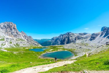 Dolomitlerin güneşli yaz gününün tadını çıkaran bir turistle birlikte Tre cime di lavaredo 'nun ve etrafındaki göllerin nefes kesici manzarası. Laghi dei Piani