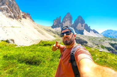 Yürüyüşçü, İtalyan dolomitlerindeki tre cime di lavaredo manzarasının tadını çıkarırken baş parmak işareti yapıyor.