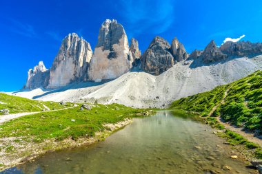 Dolomitlerde güneşli bir yaz gününde Tre cime di lavaredo 'nun ve bir dağ gölündeki yansımasının manzarası.