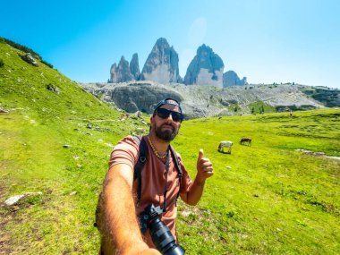 Fotoğrafçı, Tre cime di lavaredo, dolomitler, İtalya 'da bir patikada yürürken baş parmağıyla selfie çekiyor.