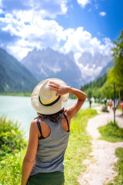 Hasır şapkasını tutan turist, yazın İtalya 'nın Durrensee Gölü' ndeki lago di Landro 'ya yansıyan dolomit dağlarının nefes kesici manzarasına hayran kalarak...