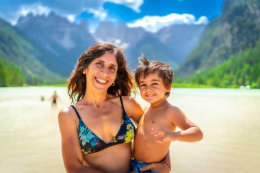 Anne ve oğul gülümseyip yaz tatilinin tadını çıkarırken İtalyan dolomitleri içinde lago di landro manzarasında yüzüyorlar.