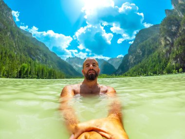 Tourist swimming in the crystal clear waters of lago di landro, surrounded by the breathtaking scenery of the dolomites on a sunny summer day clipart