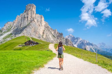 Çakıllı bir yolda yürüyen dişi turist, Meksika zirvesinin ve İtalyan dolomitlerindeki Giau geçidinin yakınındaki dağ sığınağının manzarasının tadını çıkarıyor.