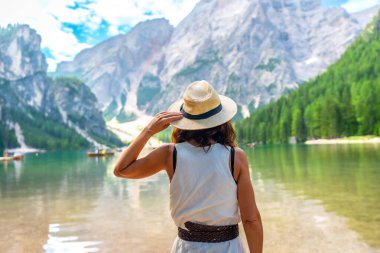 Hasır şapka takan kadın, dolomitlerle yaz tatili boyunca arka planda dağlar ve botlarla muhteşem göl manzarasına hayran kaldı.