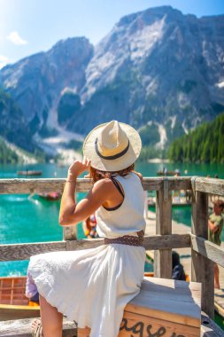 Hasır şapka takan genç bir kadın güneşli bir yaz gününde İtalyan dolomitlerinde Braies Gölü 'nün büyüleyici manzarasına hayran kaldı.