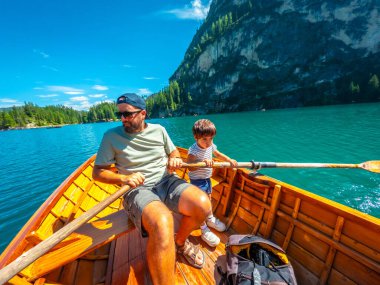 Baba ve oğul, arka planda çarpıcı dolomitlerle birlikte Braies Gölü 'nde tahta bir teknede kürek çekiyorlar.