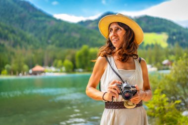 Hasır şapkalı kadın elinde klasik kamerayla dolomitlerdeki Dobbiaco Gölü 'nde yaz tatilinin tadını çıkarıyor.