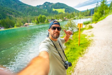 Turist Dobbiaco Gölü 'nde selfie çekiyor. Etrafı nefes kesici dağlarla çevrili. İtalyan dolomitlerinde yaz tatilinin tadını çıkarıyor.