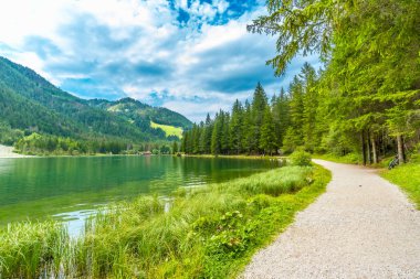 Zümrüt yeşili sular etrafındaki dağları ve yemyeşil bitki örtüsünü yansıtıyor. Dolomitlerin kalbinde huzur dolu bir manzara yaratıyor.
