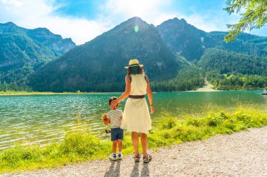 Turistler, dolomitlerin güneşli bir yaz gününde dağlarla çevrili turkuaz sularıyla Dobbiaco Gölü 'nün nefes kesici manzarasının keyfini çıkarıyorlar.