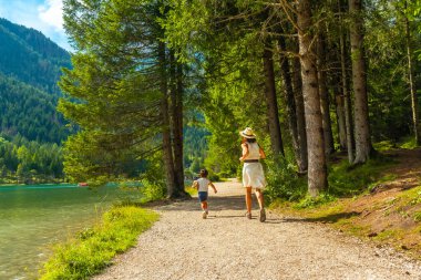 Anne ve oğlu ormandaki göl kenarında çakıllı bir patika boyunca koşuyor, dolomitlerde yaz tatilinin tadını çıkarıyorlar.
