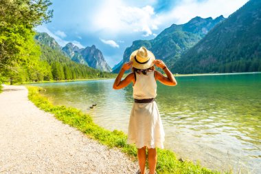 Hasır şapkasını tutan turist, yazın Dobbiaco Gölü ve Dolomite Dağları 'nın büyüleyici manzarasına hayran kaldı.