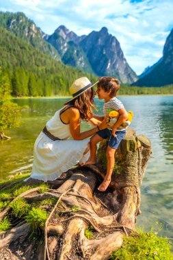 Anne ve oğlu, nefes kesen dağ manzarasıyla çevrili güzel bir alp gölünün kıyısında kaynaşıyor.