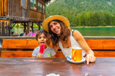 Turistler İtalyan Alplerinde bir dağ gölünün kenarında dondurma ve kahveyle yaz gününün tadını çıkarıyorlar.