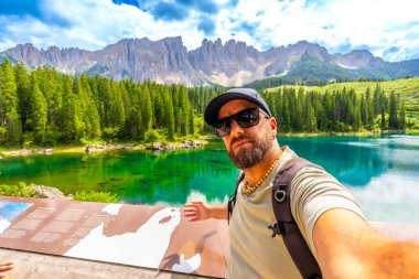 Carezza Gölü 'nde selfie çeken bir turist. Arka planda büyüleyici gecikme kitlesi ve pitoresk dolomitlerle.