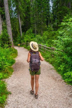 Sırt çantalı bir kadın yaz günü Carezza Gölü 'nün yanındaki yolda yürüyor. Dolomitler, İtalya.