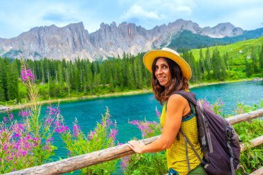 Sırt çantası ve hasır şapkalı kadın turist dolomitlerdeki Carezza Gölü ve latemar Dağı manzarasının tadını çıkarıyor. İtalyan Alpleri.