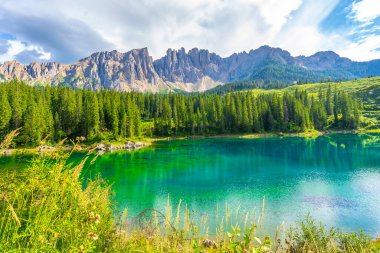 Zümrüt suları, geç kalan grubu ve etrafındaki çam ormanlarını yansıtıyor. Yazın Karersee 'de bulutlarla mavi bir gökyüzünün altında.