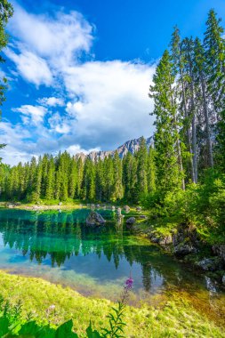 Zümrüt su, yaz aylarında Karersee 'de lago di carezza' da mavi gökyüzünün altındaki latemar sıradağlarını ve çam ormanlarını yansıtır.