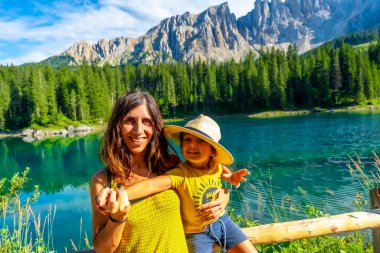 Anne ve oğul gülümsüyor ve yaz tatillerini arka planda geç dönem dağ sıraları olan Carezza gölünde geçiriyorlar.