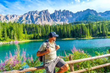 Güneşli bir yaz gününde İtalya 'nın görkemli dolomitlerle çevrili Carezza Gölü' nün büyüleyici turkuaz sularına hayran olan yürüyüşçü.