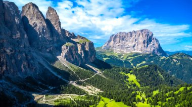 Dolomitlerde nefes kesen yaz manzarası, yemyeşil vadilerden ve yüksek zirvelerden geçen dolambaçlı bir yol.