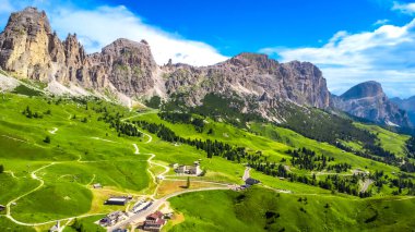 Dolomitlerdeki manzaralı bahçe geçidinin nefes kesen manzarası, dolambaçlı yollar, yeşil vadiler ve parlak mavi gökyüzünün altındaki görkemli zirveler.