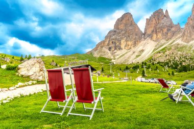 Kırmızı şezlonglar turistleri dinlenmeye ve dolomitlerdeki Sassolungo dağının nefes kesen manzarasının tadını çıkarmaya davet ediyor.