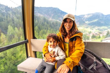 Turistler İtalyan dolomitleri içinde manzaralı bir teleferiğe binip nefes kesici dağ manzaralarını seyrediyorlar.